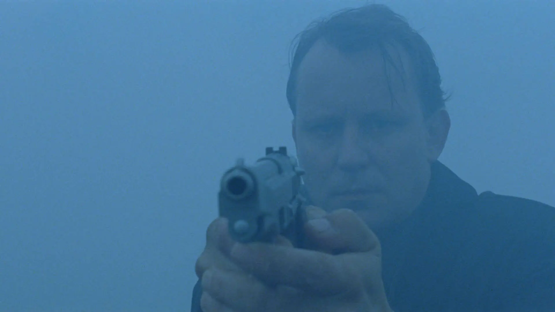 استلان اسکارزگارد ایستاده در مه با اسلحه‌ای که به سمت مقابل نشانه رفته است در نمایی از فیلم بی‌خوابی به کارگردانی اریک شولدبرگ