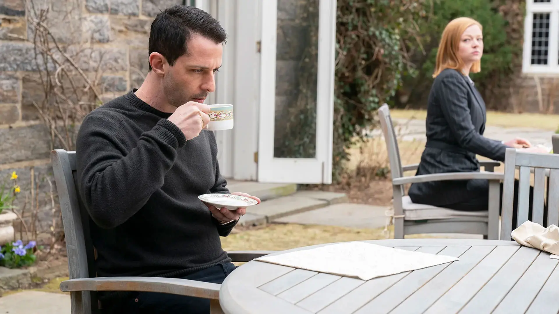 جرمی استرانگ در حال نوشیدن قهوه در حالی که سارا اسنوک دورتر دیده می‌شود در نمایی از سریال وراثت